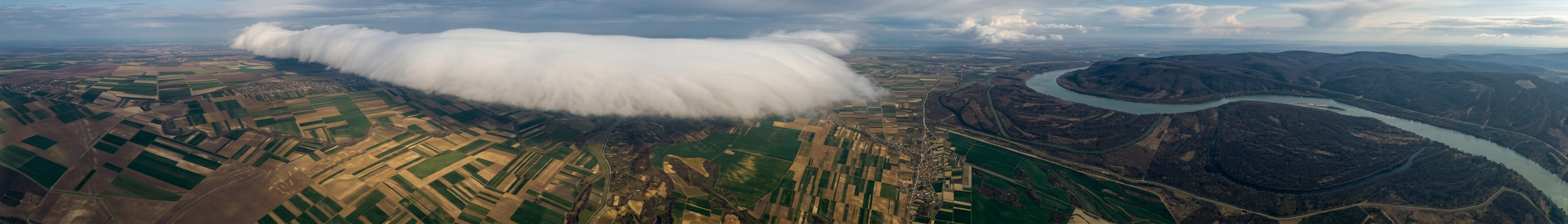 Roll cloud formation showing a long, horizontal tube-shaped arcus cloud stretching across a dark, stormy sky.