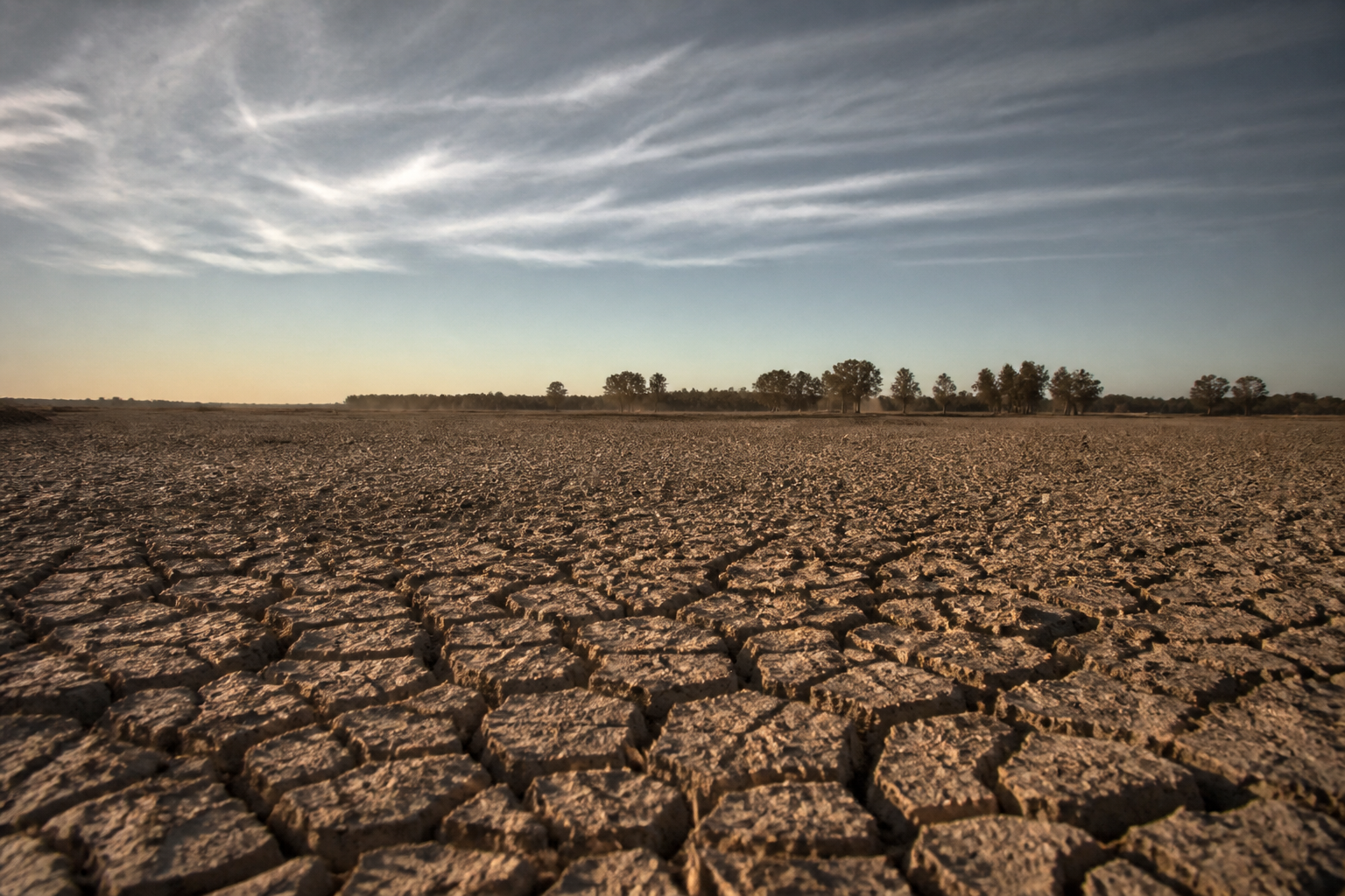 Dry, cracked soil beneath a thin layer of clouds illustrating drought conditions.