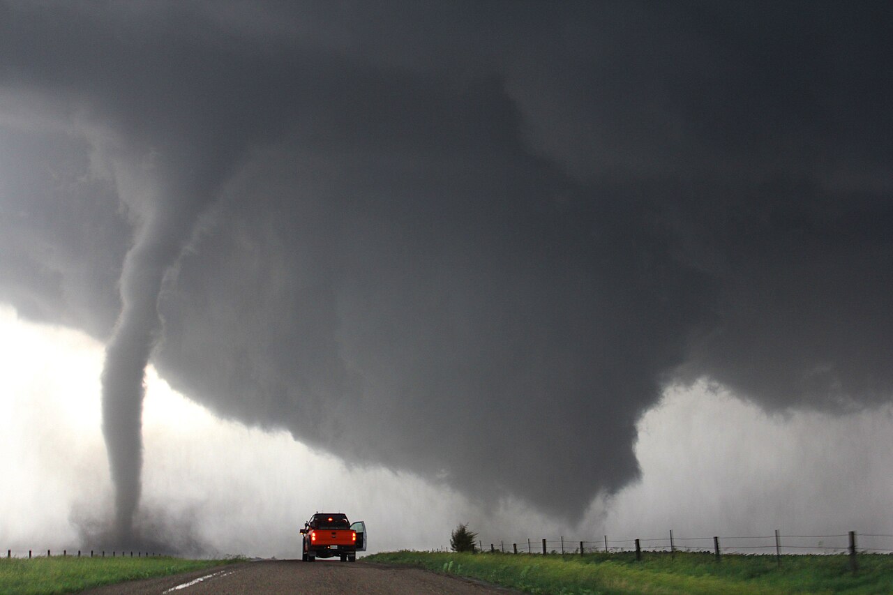Supercell tornado formation visualised with a dark rotating storm cloud, lightning and a funnel touching the ground.