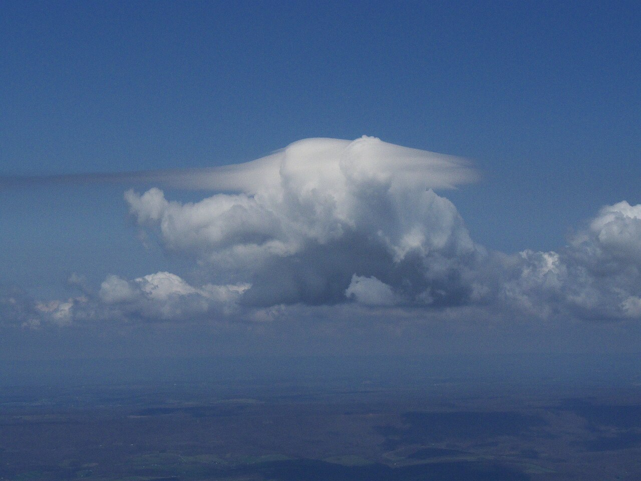A white pileus cloud, or storm cap, forming above a cumulus cloud against a blue sky, demonstrating cloud formation. A white pileus cloud, or storm cap, forming above a cumulus cloud against a blue sky, demonstrating cloud formation.