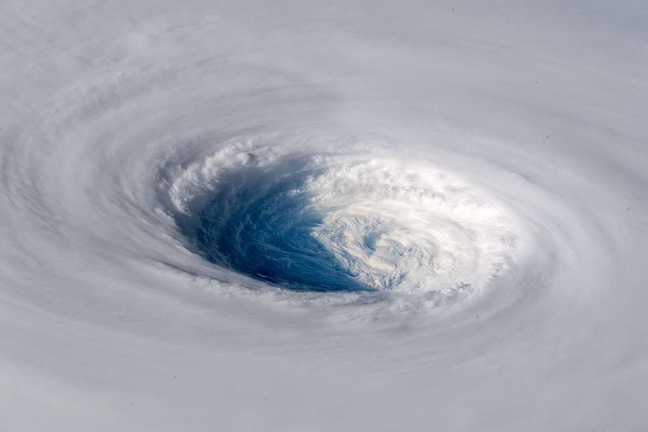 Aerial view of a hurricane's clear, dark blue eye surrounded by swirling white clouds, illustrating eye formation.
