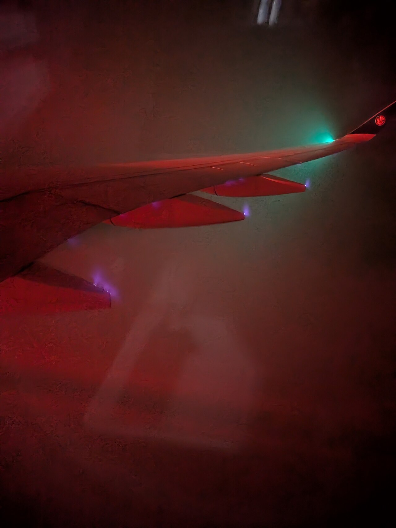 Airplane wing in dark, cloudy sky with glowing purple/blue St. Elmo's Fire on its surface, explaining atmospheric physics. Airplane wing in dark, cloudy sky with glowing purple/blue St. Elmo's Fire on its surface, explaining atmospheric physics.