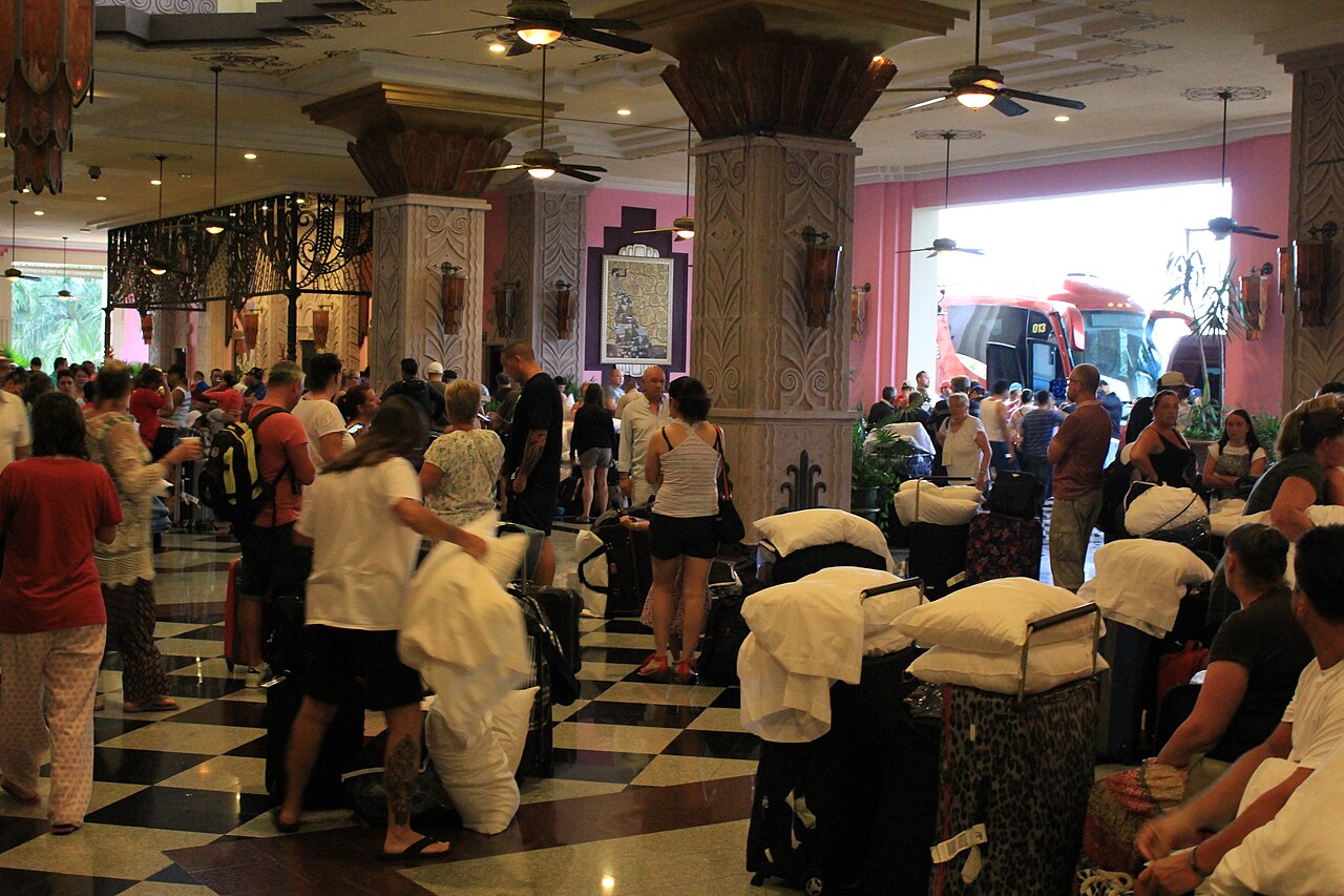 Crowd of people and luggage in a hotel lobby, evacuating from Hurricane Patricia as buses wait outside.