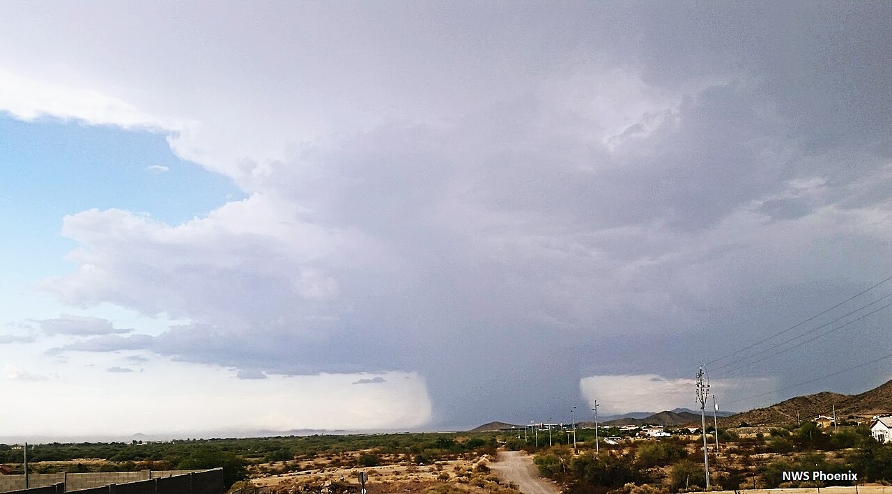 Developing microburst downdrafts from a severe thunderstorm over a desert landscape with mountains and scattered buildings. Developing microburst downdrafts from a severe thunderstorm over a desert landscape with mountains and scattered buildings.