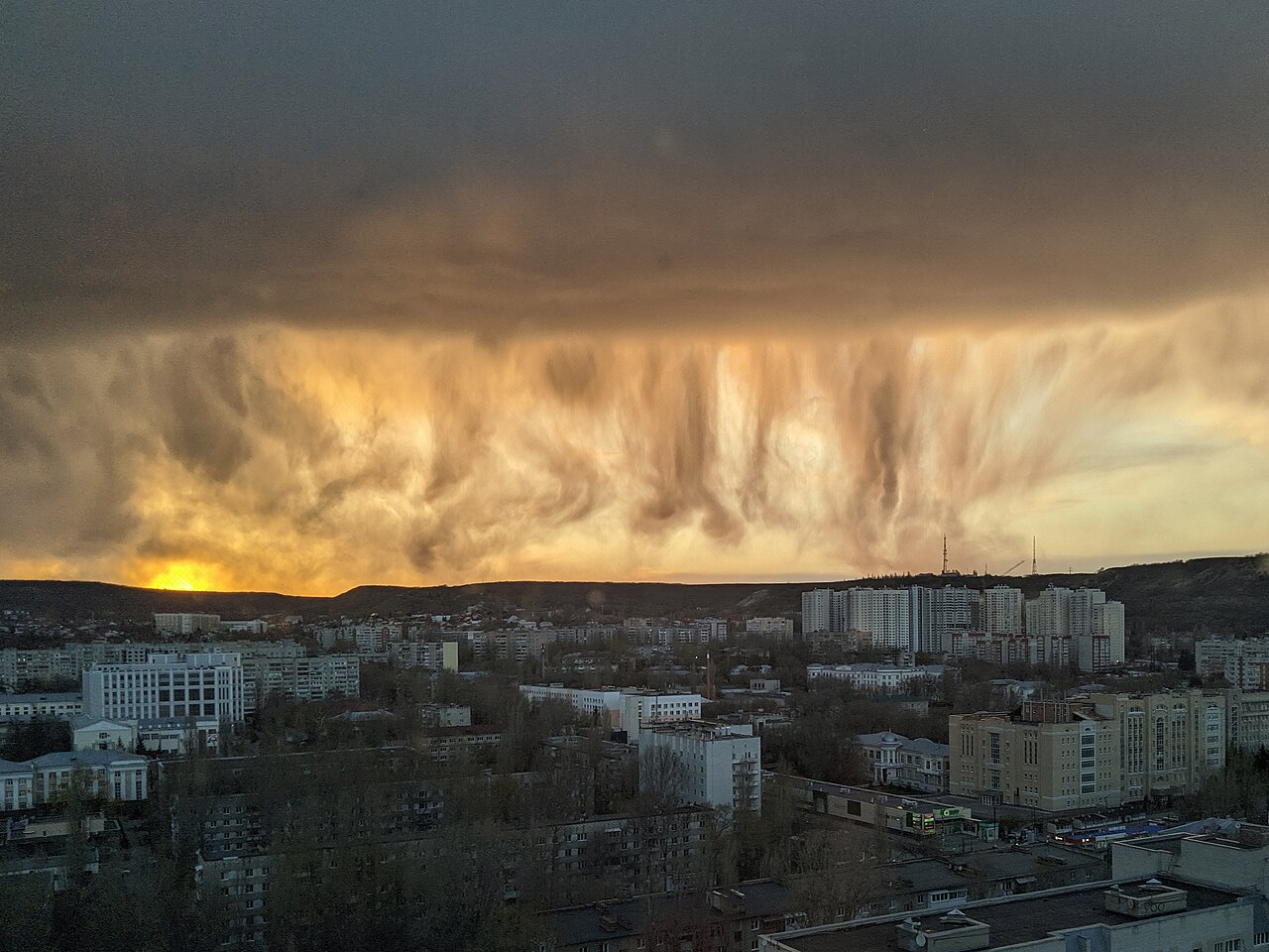 Golden virga streaks from dark clouds over a city at sunset, illustrating evaporating precipitation. Golden virga streaks from dark clouds over a city at sunset, illustrating evaporating precipitation.