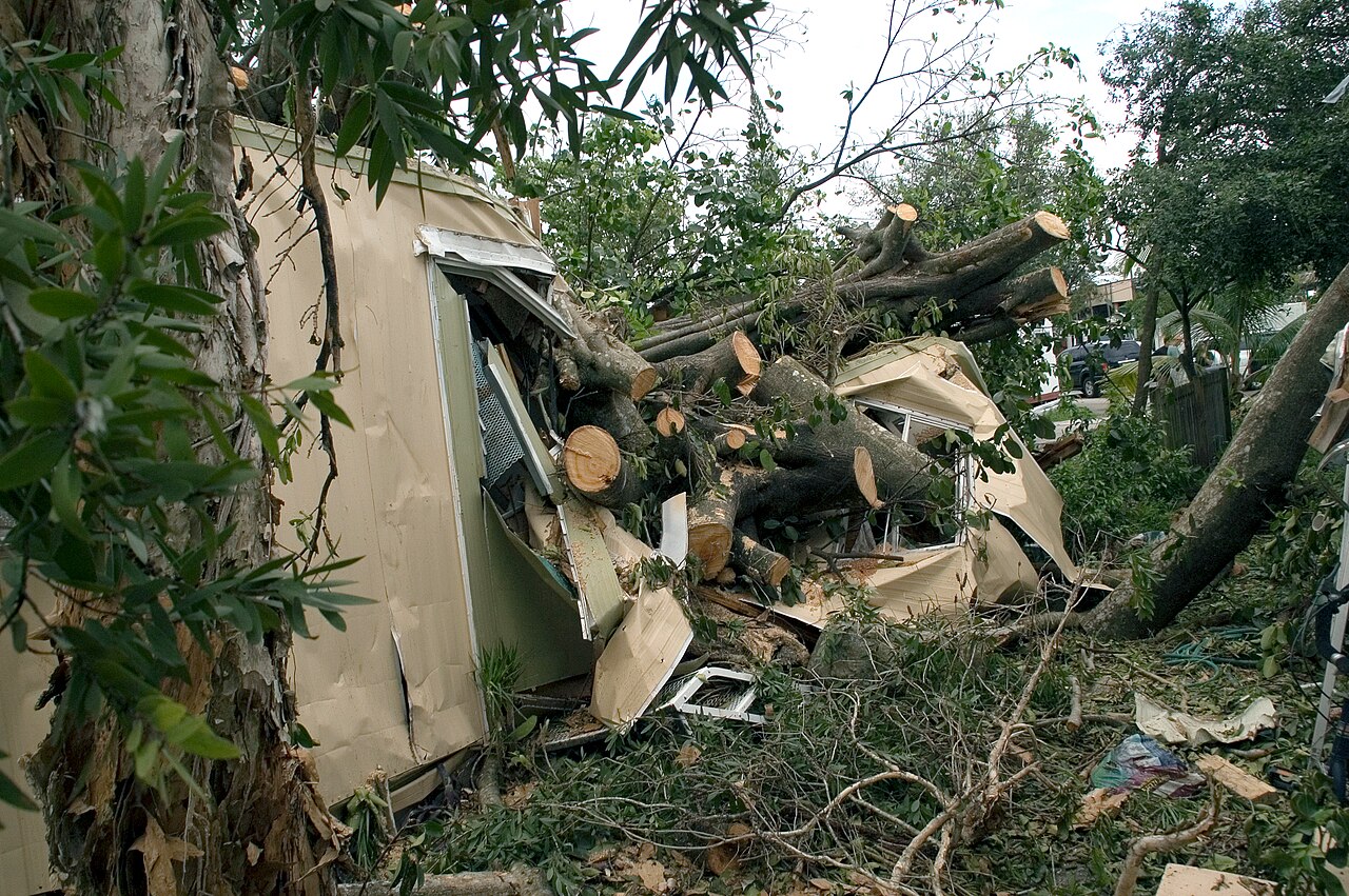 Hurricane Katrina damage: a mobile home crushed by large, cut tree trunks and debris, highlighting structural failures. Hurricane Katrina damage: a mobile home crushed by large, cut tree trunks and debris, highlighting structural failures.