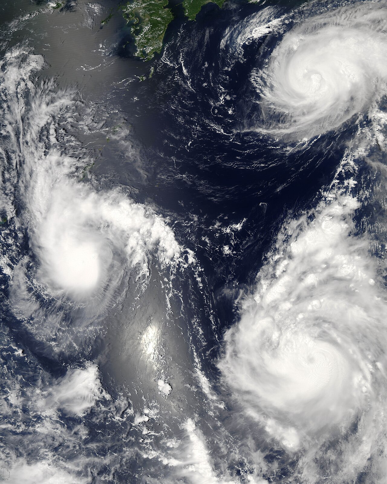 Satellite view of three swirling hurricanes over dark ocean, illustrating how these powerful storms form. Satellite view of three swirling hurricanes over dark ocean, illustrating how these powerful storms form.
