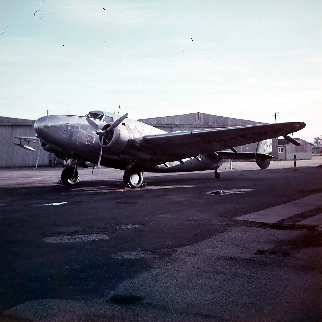 Silver twin-engine propeller plane, used for cloud seeding, parked on an airfield tarmac near hangars. Silver twin-engine propeller plane, used for cloud seeding, parked on an airfield tarmac near hangars.