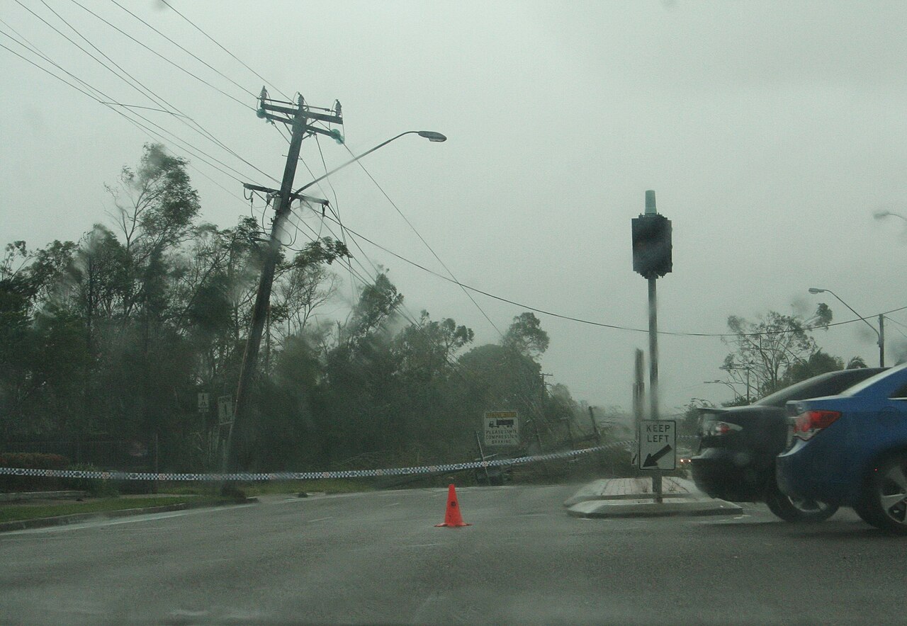Street after a tropical cyclone: downed power lines, bent trees, and debris from strong winds and heavy rain. Street after a tropical cyclone: downed power lines, bent trees, and debris from strong winds and heavy rain.