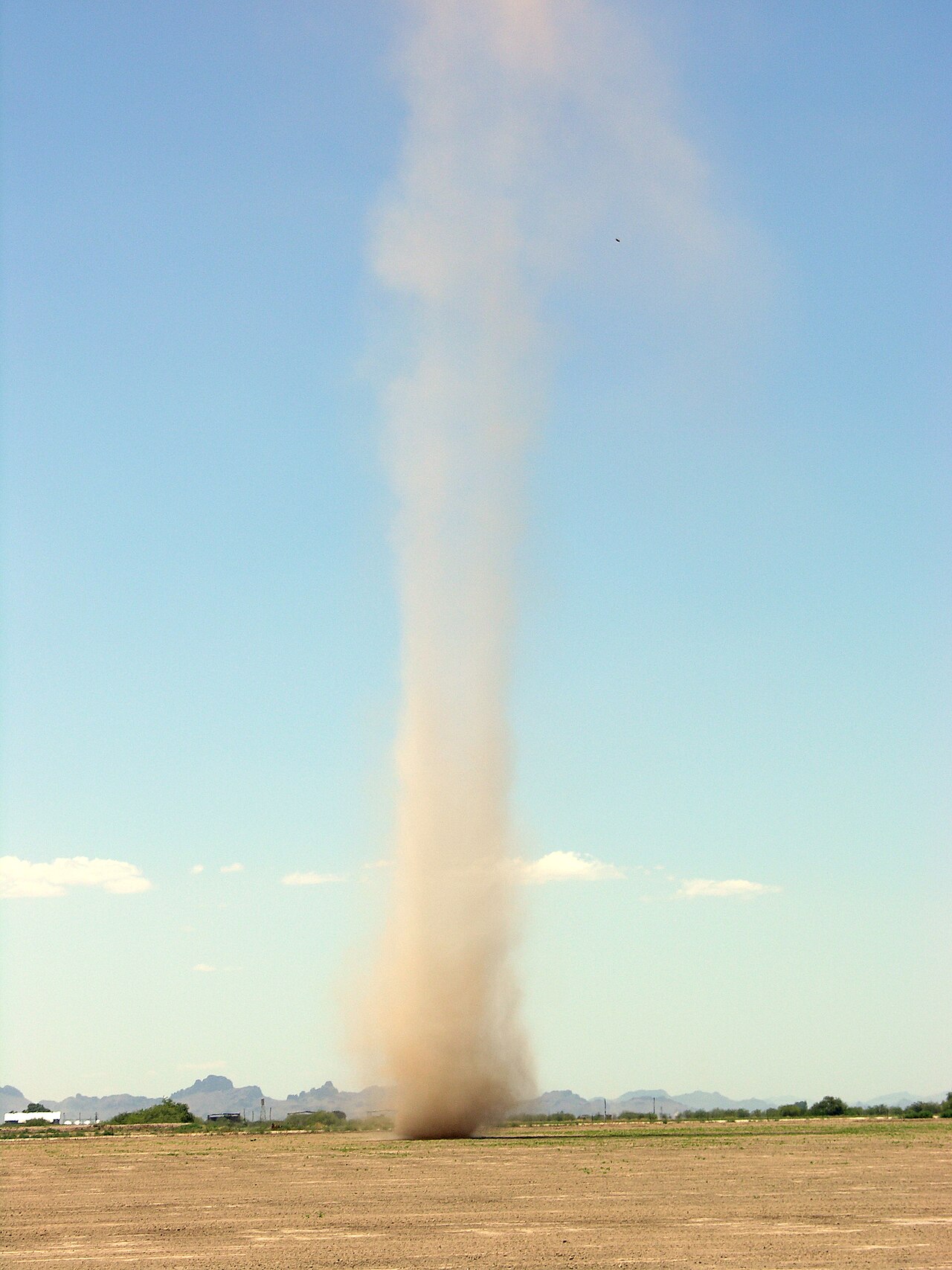 Tall dust devil swirling dust in a dry, open field under a clear blue sky, illustrating whirlwind formation. Tall dust devil swirling dust in a dry, open field under a clear blue sky, illustrating whirlwind formation.