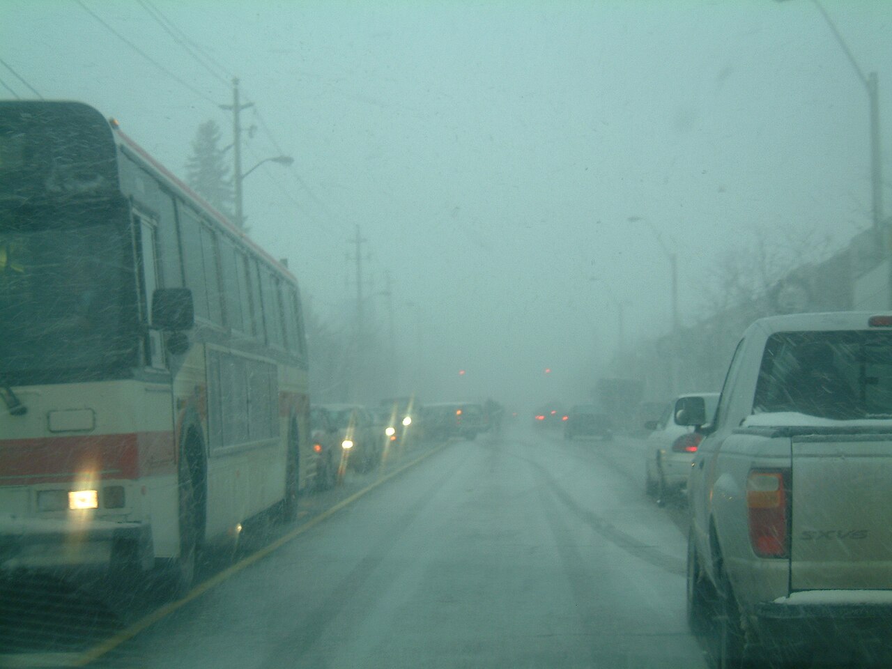 Vehicles on a highway during a snow squall whiteout, with a bus and pickup truck visible through heavy snowfall.