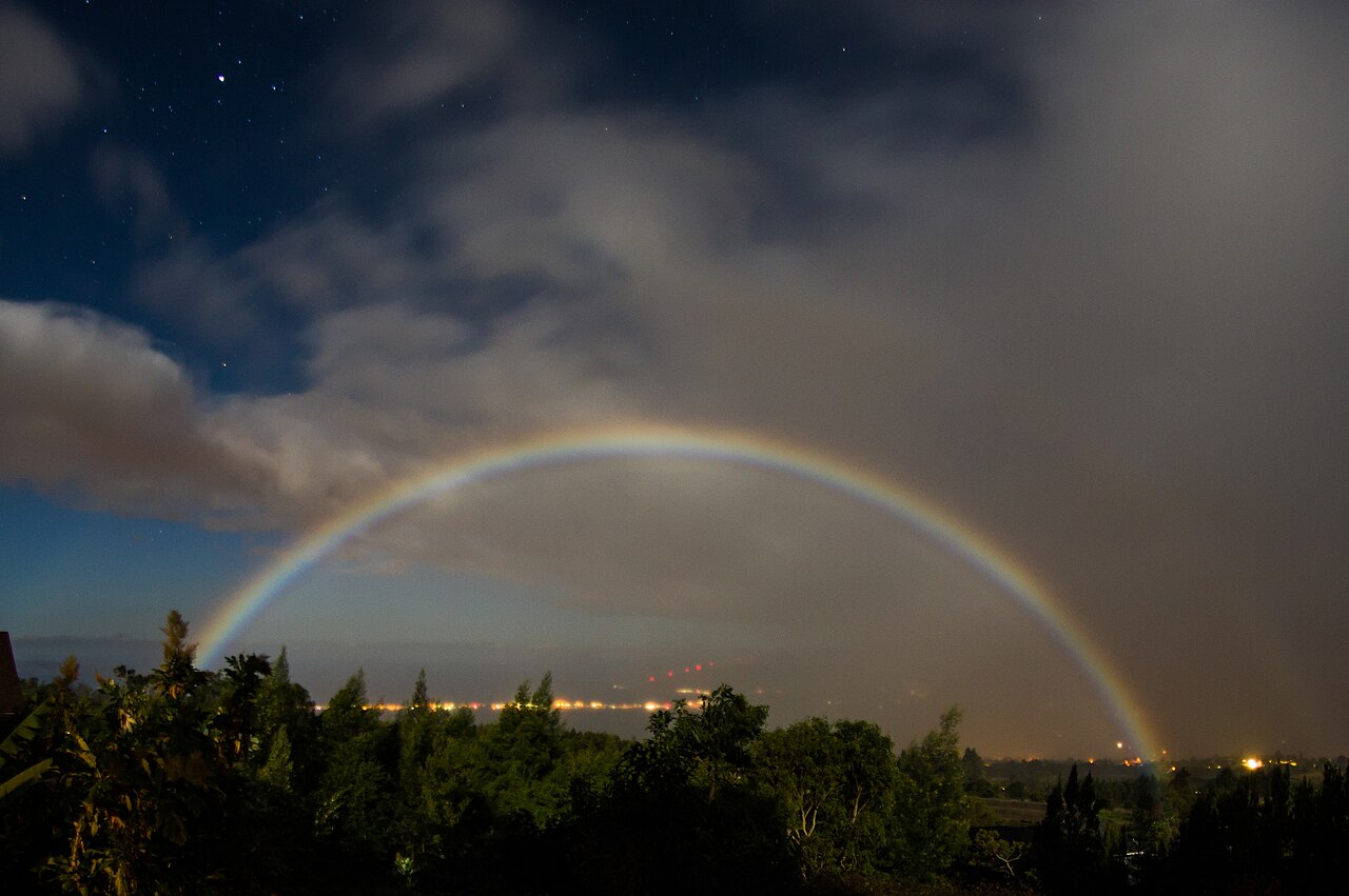 Vibrant moonbow arching over a dark landscape with city lights, illustrating optimal conditions for viewing. Vibrant moonbow arching over a dark landscape with city lights, illustrating optimal conditions for viewing.