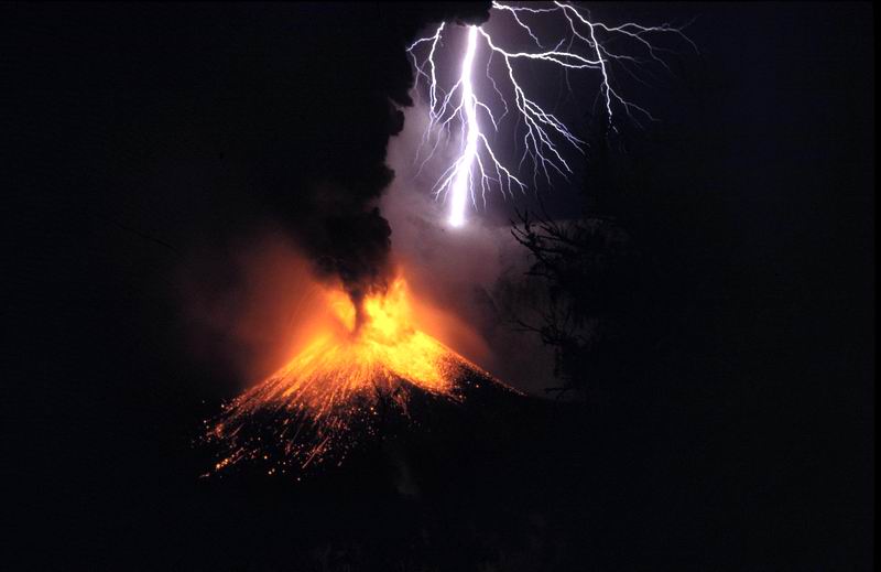 Volcanic lightning strikes through a dark ash cloud above an erupting volcano, illustrating ash cloud electrification. Volcanic lightning strikes through a dark ash cloud above an erupting volcano, illustrating ash cloud electrification.